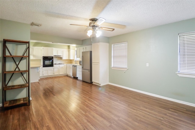 kitchen featuring appliances with stainless steel finishes, a ceiling fan, white cabinets, wood finished floors, and baseboards