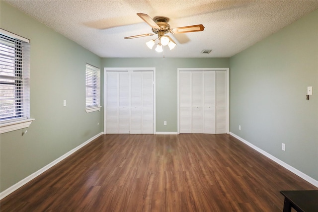 unfurnished bedroom with wood finished floors, visible vents, baseboards, and two closets