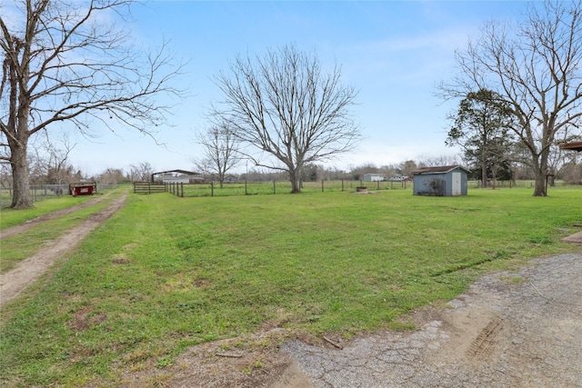 view of yard featuring a storage shed, a rural view, fence, and an outbuilding