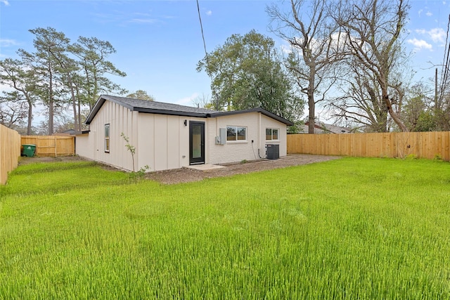 back of property with central AC unit, a fenced backyard, a yard, board and batten siding, and brick siding