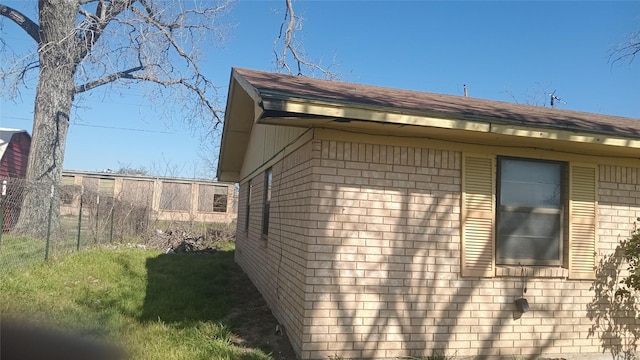 view of home's exterior with a yard, brick siding, a shingled roof, and fence