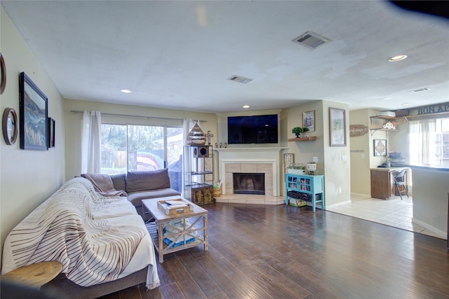 living room featuring a tile fireplace, recessed lighting, wood finished floors, visible vents, and baseboards