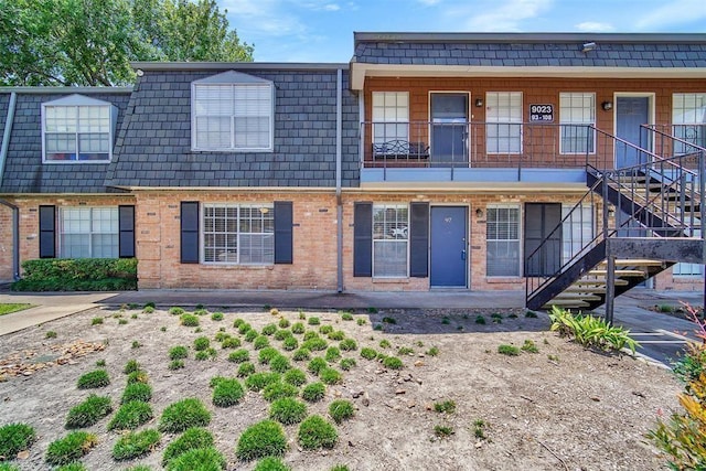 townhome / multi-family property with stairway, mansard roof, and brick siding