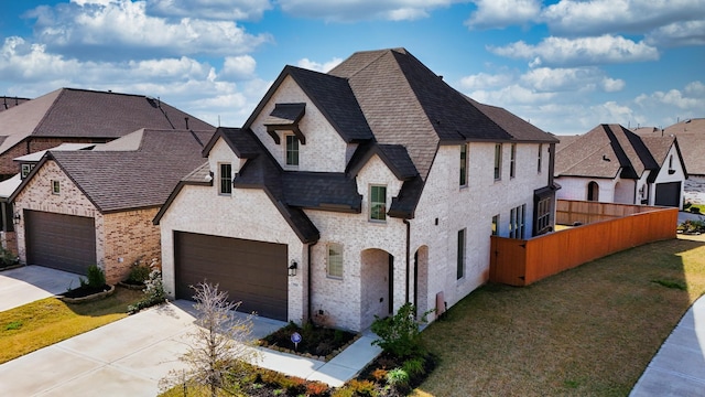 french country inspired facade featuring an attached garage, a shingled roof, fence, concrete driveway, and a front yard