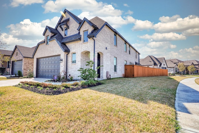 french country inspired facade with an attached garage, fence, concrete driveway, and a front yard