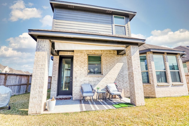 rear view of house featuring a yard, brick siding, a patio area, and fence