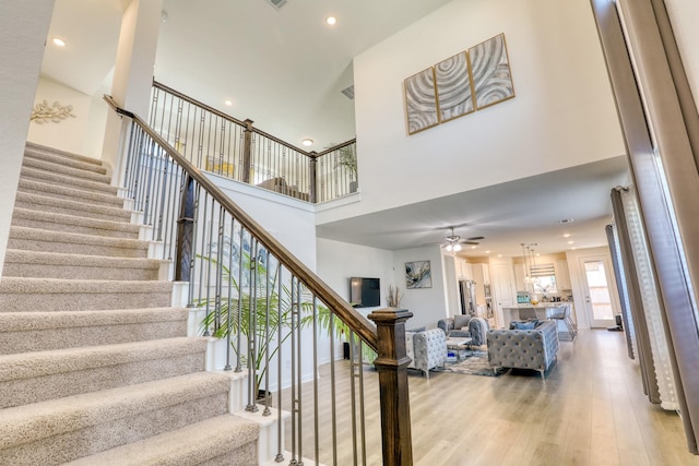 stairway featuring recessed lighting, a high ceiling, a ceiling fan, wood finished floors, and baseboards