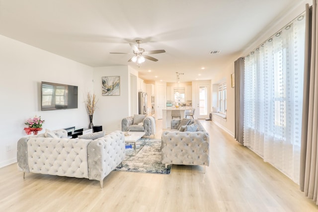 living area featuring baseboards, ceiling fan, visible vents, and light wood-style floors