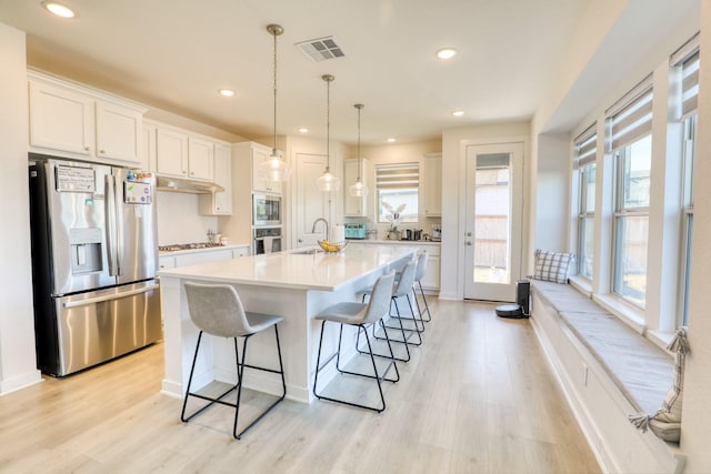 kitchen featuring a breakfast bar area, stainless steel appliances, light countertops, visible vents, and white cabinets