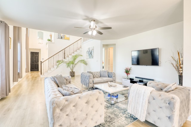 living room with light wood-style floors, ceiling fan, stairway, and baseboards