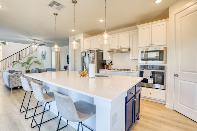 kitchen with stainless steel appliances, visible vents, backsplash, light wood-style floors, and under cabinet range hood