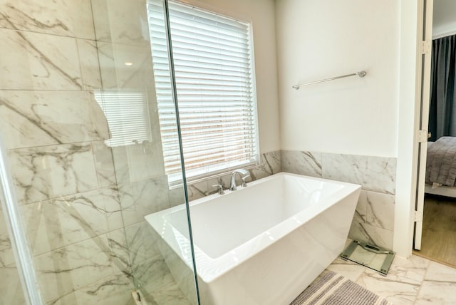 bathroom featuring marble finish floor, tile walls, and a soaking tub