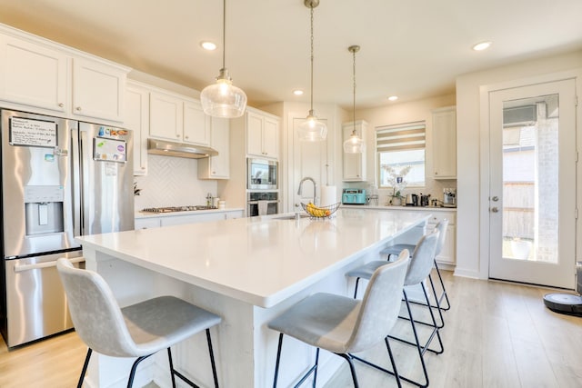 kitchen with stainless steel appliances, a breakfast bar, a sink, and under cabinet range hood