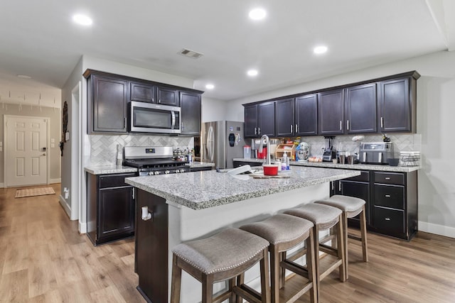 kitchen featuring a breakfast bar area, light wood-style flooring, stainless steel appliances, visible vents, and a center island with sink