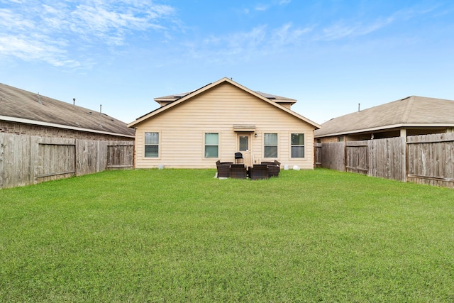 back of property with a fenced backyard, roof mounted solar panels, and a yard