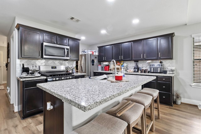 kitchen with a breakfast bar, a center island with sink, stainless steel appliances, visible vents, and light wood-style flooring