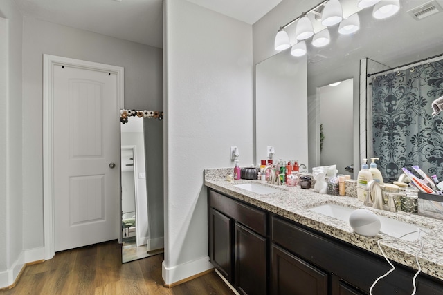 full bathroom with double vanity, visible vents, a sink, and wood finished floors