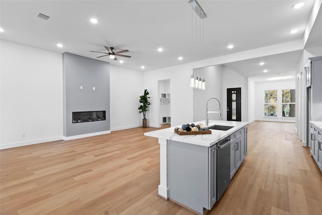 kitchen featuring dishwasher, a fireplace, a sink, and gray cabinetry