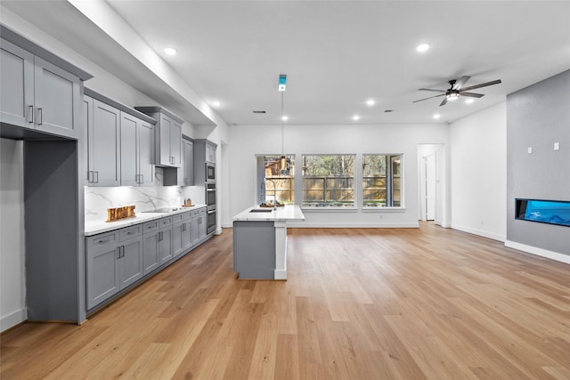 kitchen with gray cabinets, light countertops, a ceiling fan, open floor plan, and light wood-type flooring