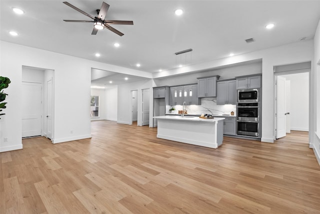 kitchen featuring light countertops, backsplash, gray cabinetry, appliances with stainless steel finishes, and open floor plan