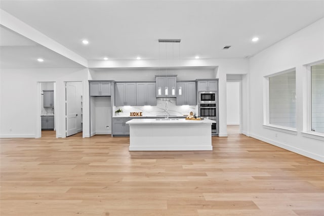 kitchen with built in microwave, gray cabinetry, light wood-style floors, light countertops, and decorative backsplash