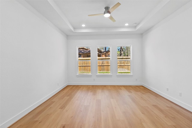 empty room with light wood finished floors, baseboards, and a raised ceiling