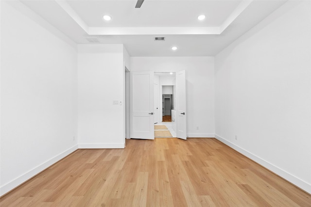 unfurnished bedroom with a tray ceiling, visible vents, light wood finished floors, and baseboards