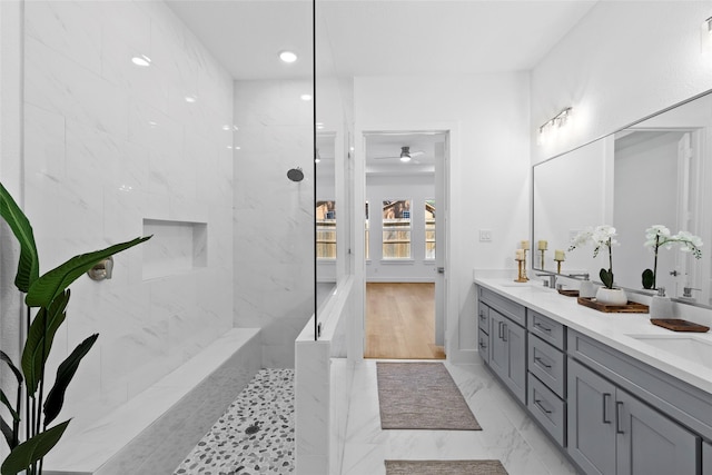 full bathroom featuring marble finish floor, tiled shower, a sink, and double vanity