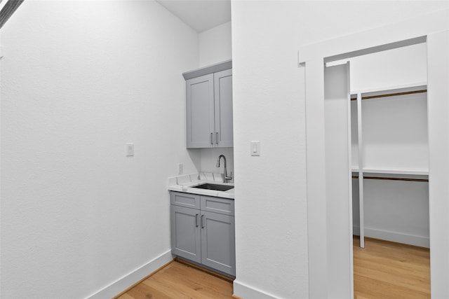 bar with a sink, light wood-style flooring, and baseboards