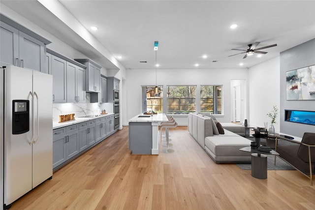 kitchen with gray cabinetry, open floor plan, light countertops, appliances with stainless steel finishes, and a kitchen bar