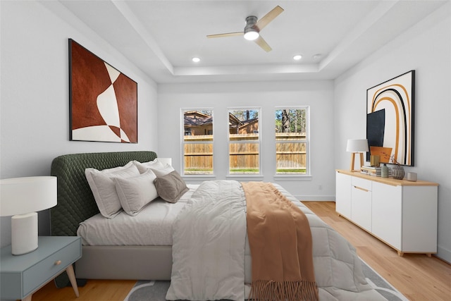 bedroom with light wood-style floors, a tray ceiling, and recessed lighting