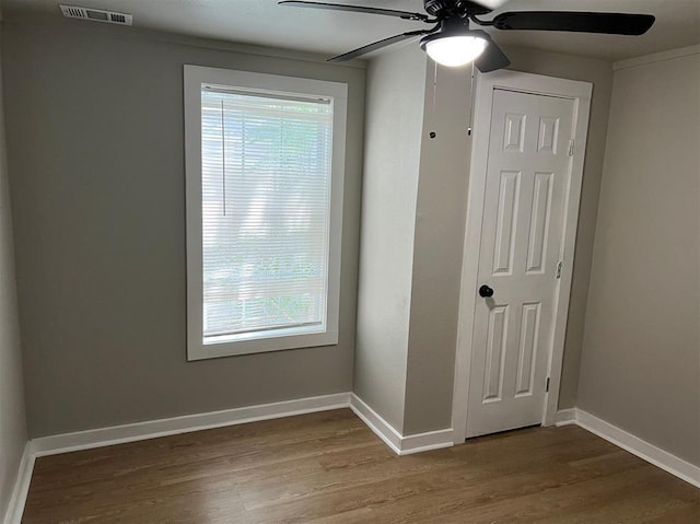 spare room with a ceiling fan, visible vents, baseboards, and wood finished floors