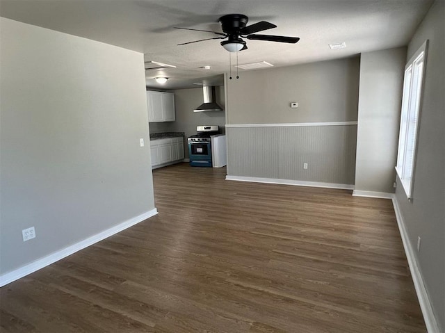 unfurnished living room with ceiling fan, a wainscoted wall, dark wood finished floors, and baseboards