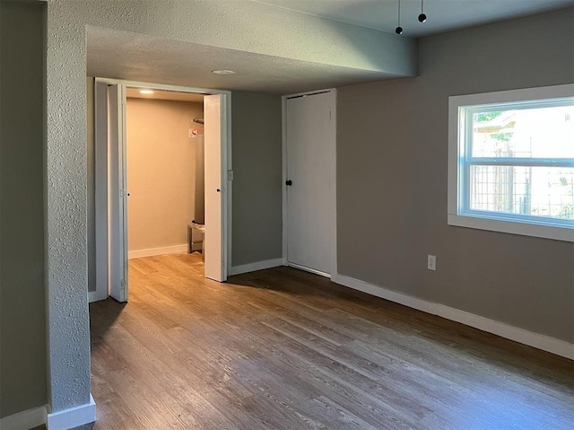 unfurnished room featuring a textured ceiling, baseboards, and wood finished floors