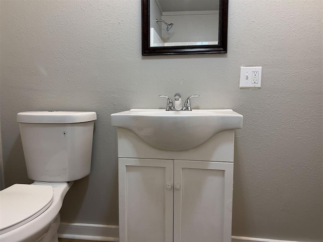 bathroom featuring a textured wall, vanity, toilet, and baseboards