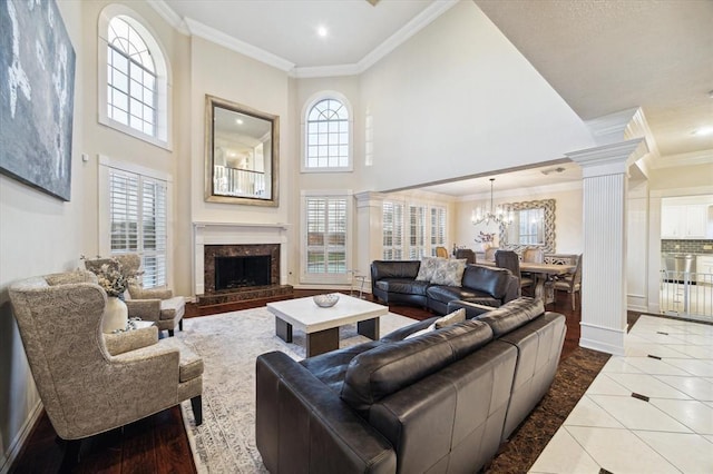 tiled living room with decorative columns, a towering ceiling, crown molding, a chandelier, and a high end fireplace