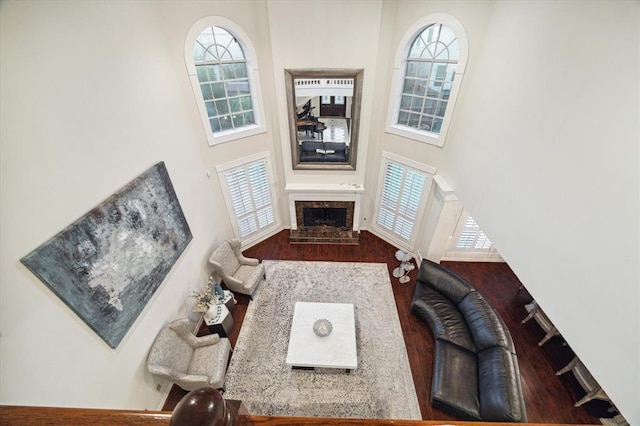 living room with a fireplace with raised hearth, wood finished floors, and a towering ceiling