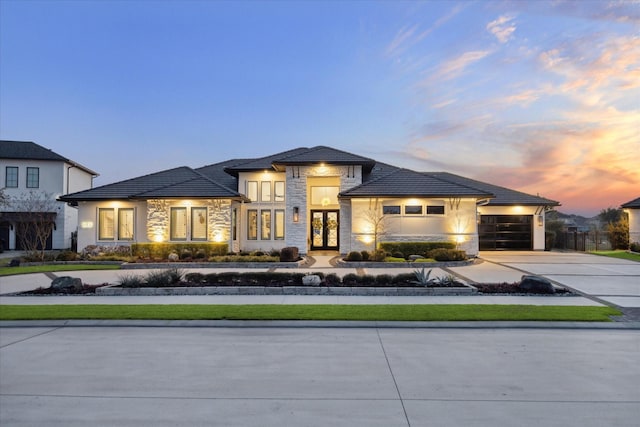 prairie-style home featuring a garage, concrete driveway, french doors, stone siding, and stucco siding