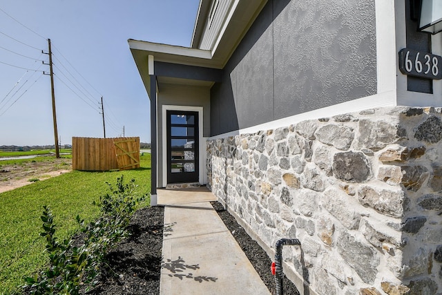 doorway to property featuring stone siding and fence