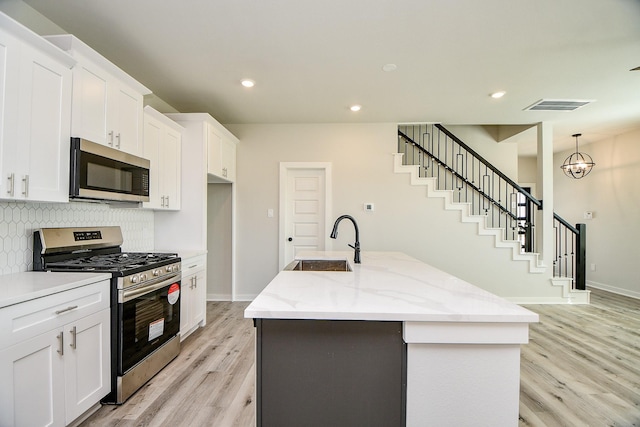 kitchen with tasteful backsplash, visible vents, appliances with stainless steel finishes, a kitchen island with sink, and a sink