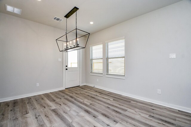 unfurnished dining area featuring an inviting chandelier, baseboards, visible vents, and wood finished floors