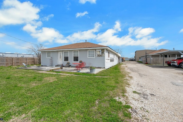 rear view of property with aphalt driveway, a patio area, fence, and a lawn