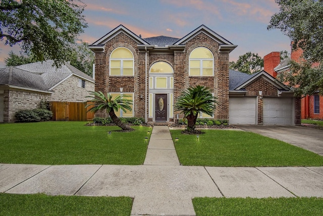 traditional-style home featuring brick siding, a yard, an attached garage, fence, and driveway