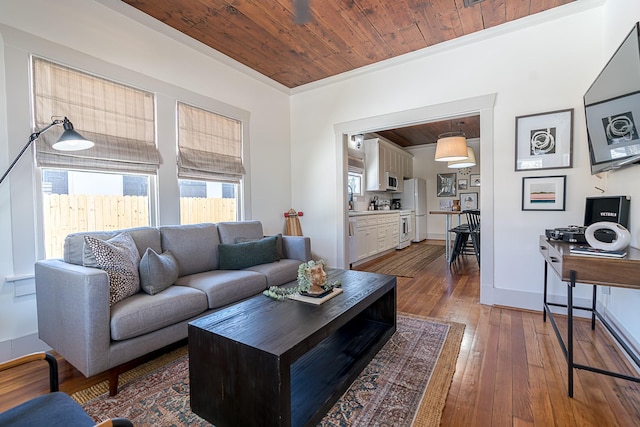 living area featuring wooden ceiling, wood-type flooring, baseboards, and ornamental molding