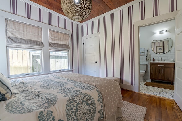 bedroom with wallpapered walls, wood-type flooring, a sink, and ensuite bathroom