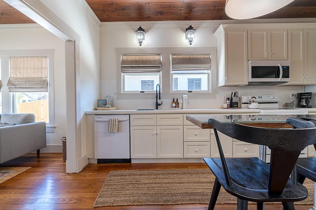 kitchen with white appliances, wood finished floors, a sink, tasteful backsplash, and crown molding