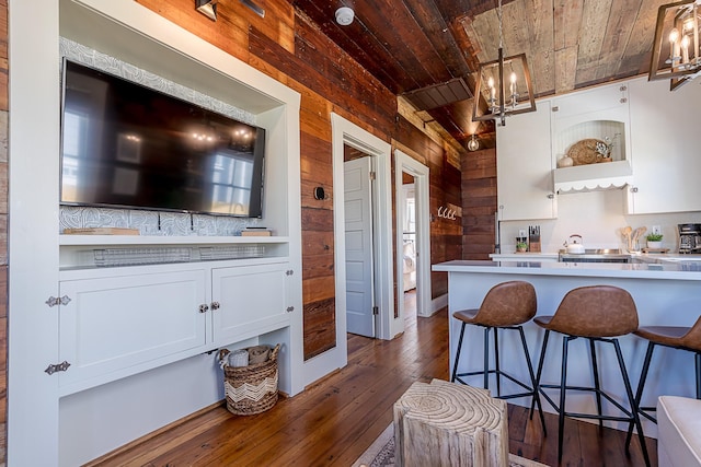 kitchen with dark wood-style flooring, a breakfast bar area, an inviting chandelier, wood ceiling, and wooden walls