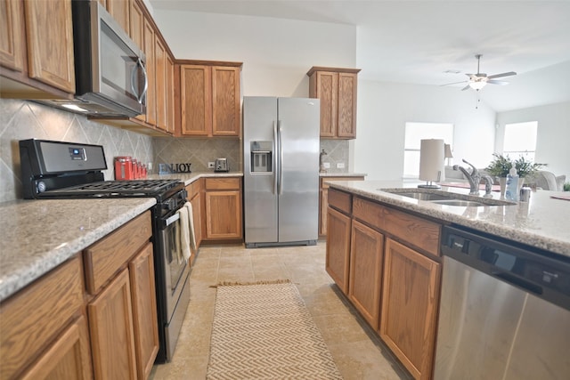 kitchen with stainless steel appliances, brown cabinetry, a sink, and light stone countertops