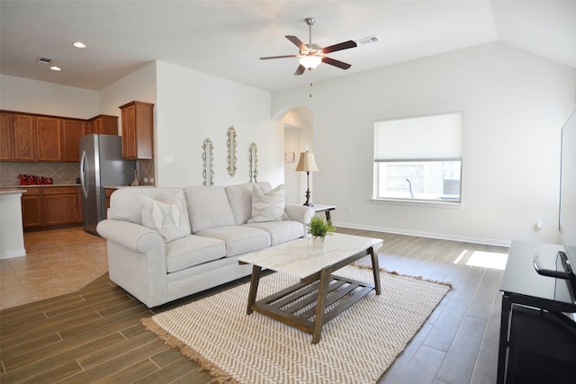 living room with arched walkways, ceiling fan, lofted ceiling, baseboards, and light wood-style floors