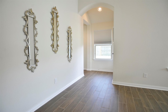 hallway featuring baseboards, arched walkways, and dark wood-style flooring